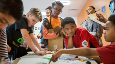 A middle school student explains the inspiration for his art project to classmates.